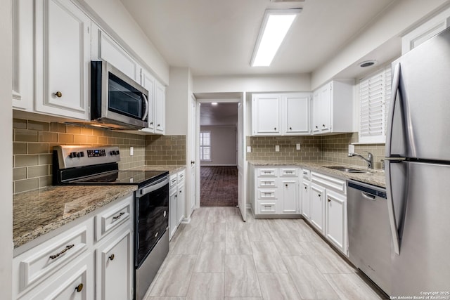 kitchen with white cabinetry, stainless steel appliances, tasteful backsplash, light stone counters, and sink