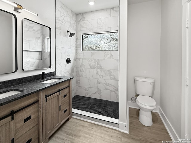 bathroom featuring toilet, hardwood / wood-style flooring, tiled shower, and vanity