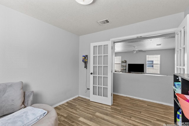 living area featuring ceiling fan, french doors, a textured ceiling, and hardwood / wood-style flooring