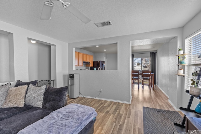 living room featuring ceiling fan, a wealth of natural light, a textured ceiling, and light wood-type flooring