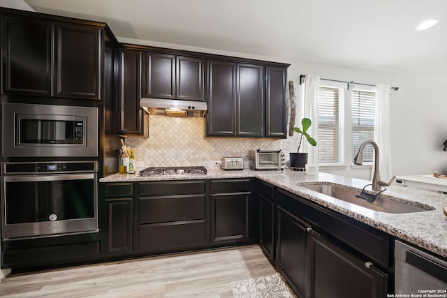 kitchen featuring light stone countertops, appliances with stainless steel finishes, decorative backsplash, sink, and light hardwood / wood-style flooring