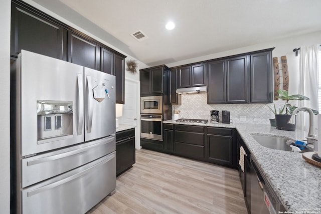 kitchen featuring light hardwood / wood-style floors, appliances with stainless steel finishes, backsplash, light stone countertops, and sink