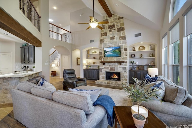 living room with built in features, beam ceiling, a stone fireplace, and a high ceiling