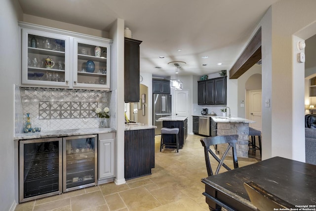 bar with wine cooler, decorative light fixtures, stainless steel appliances, light stone countertops, and backsplash