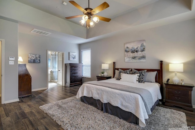 bedroom featuring ceiling fan, ensuite bath, dark hardwood / wood-style floors, and a raised ceiling