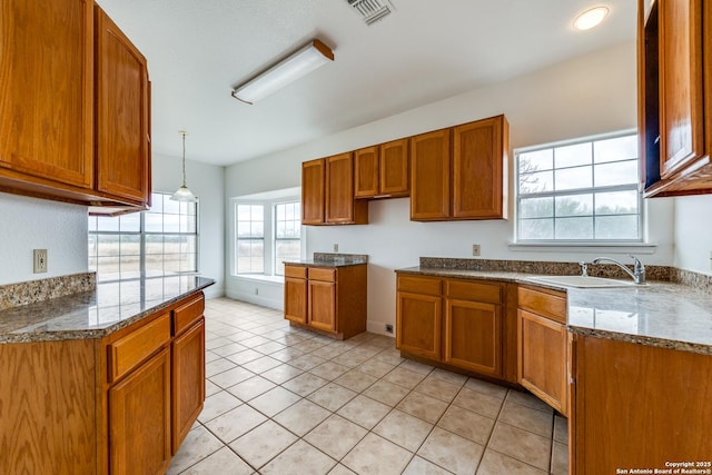 kitchen with pendant lighting, a wealth of natural light, sink, light stone counters, and light tile patterned floors