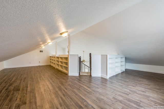 additional living space featuring vaulted ceiling, dark hardwood / wood-style flooring, and a textured ceiling