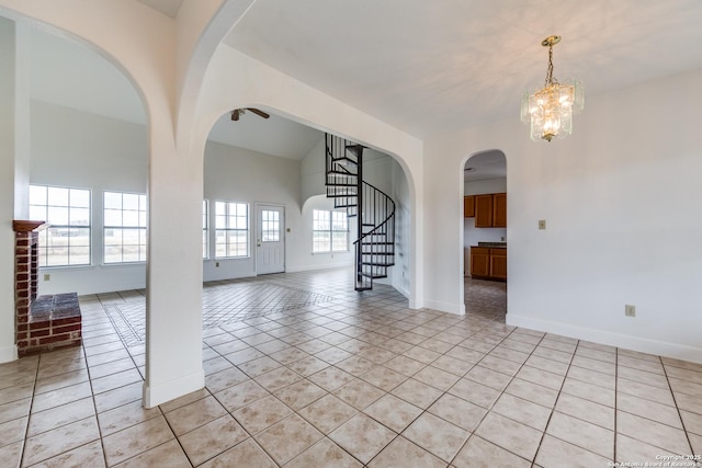 empty room with light tile patterned flooring, a brick fireplace, a chandelier, and lofted ceiling