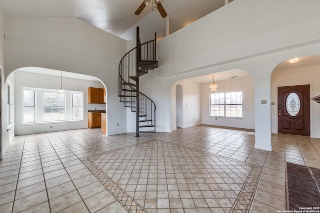 unfurnished living room with high vaulted ceiling, light tile patterned floors, and ceiling fan with notable chandelier