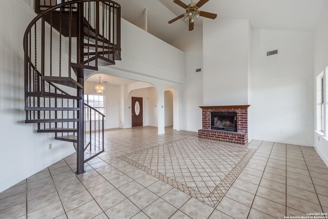 unfurnished living room with high vaulted ceiling, light tile patterned floors, a brick fireplace, and ceiling fan with notable chandelier