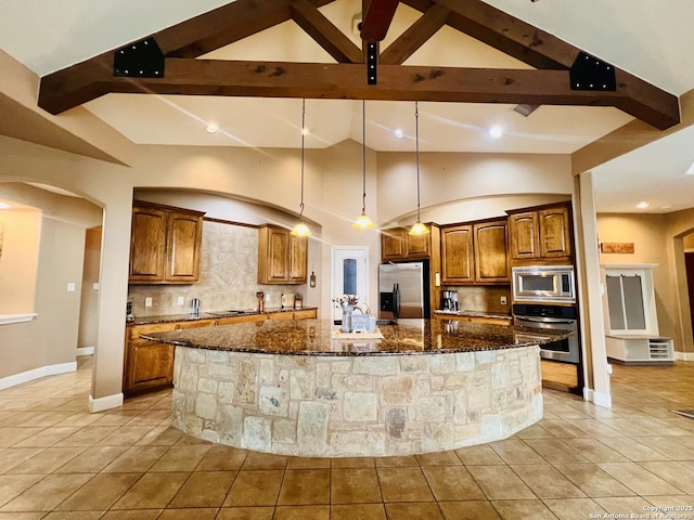 kitchen with a large island, stainless steel appliances, tasteful backsplash, decorative light fixtures, and dark stone countertops