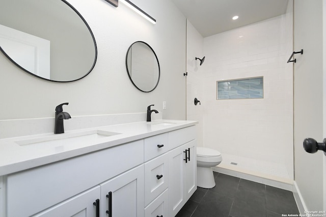 bathroom featuring double vanity, toilet, tiled shower, and a sink