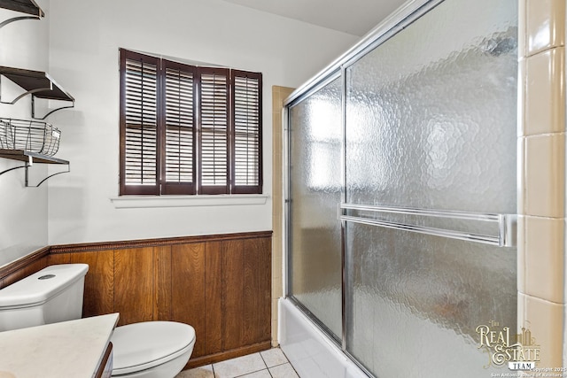 full bathroom featuring tile patterned flooring, vanity, bath / shower combo with glass door, toilet, and wood walls