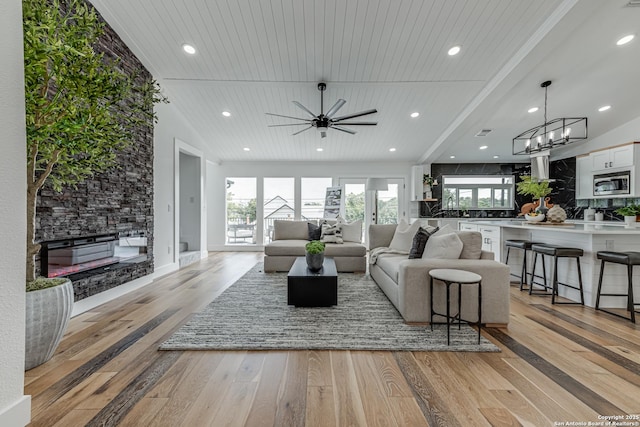 living room with vaulted ceiling, a fireplace, light hardwood / wood-style flooring, ceiling fan with notable chandelier, and wooden ceiling