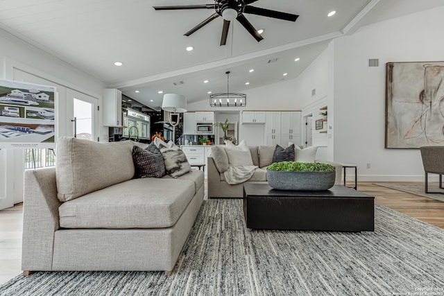 living room featuring ceiling fan with notable chandelier, lofted ceiling, ornamental molding, and light wood-type flooring