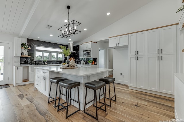 kitchen featuring stainless steel microwave, backsplash, a notable chandelier, white cabinets, and a center island