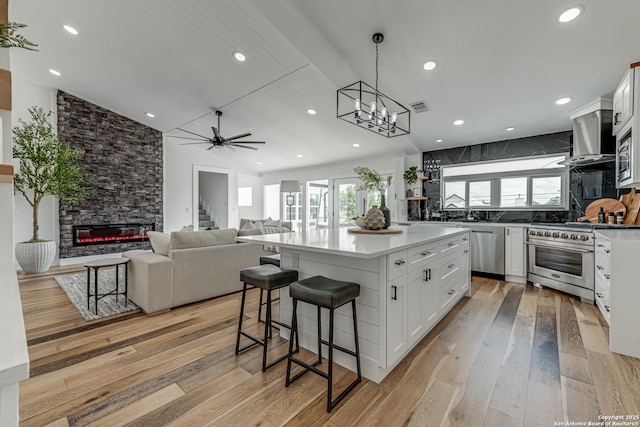 kitchen featuring white cabinetry, stainless steel appliances, lofted ceiling, wall chimney exhaust hood, and a center island