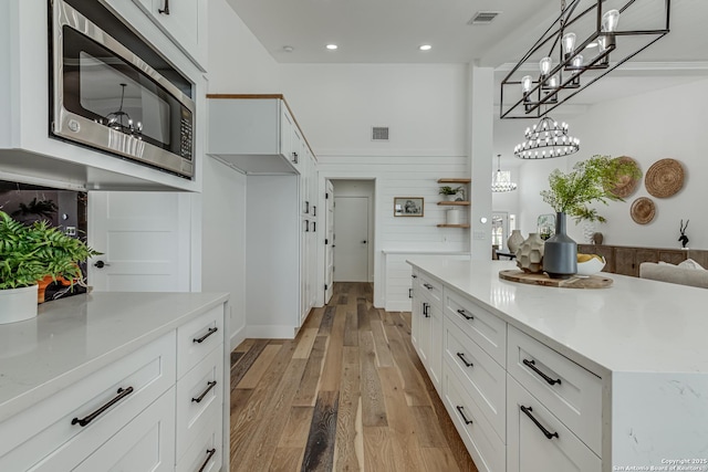 kitchen with white cabinets, light stone countertops, light hardwood / wood-style floors, and pendant lighting