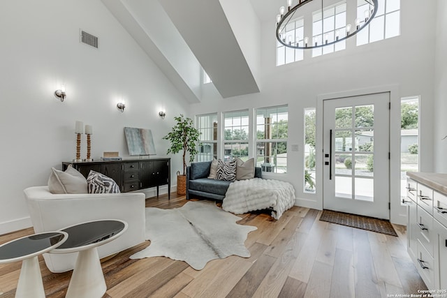 living room with light hardwood / wood-style floors, a notable chandelier, and a towering ceiling