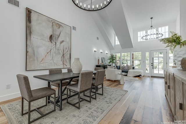 dining space featuring an inviting chandelier, a towering ceiling, and light hardwood / wood-style flooring