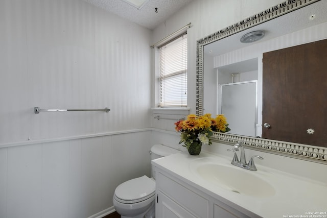 bathroom featuring toilet, wooden walls, walk in shower, a textured ceiling, and vanity