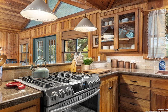 kitchen with vaulted ceiling, stainless steel gas range oven, brown cabinetry, and wooden walls