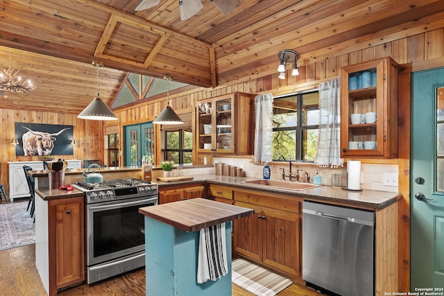 kitchen featuring wooden walls, stainless steel appliances, butcher block countertops, a peninsula, and a sink