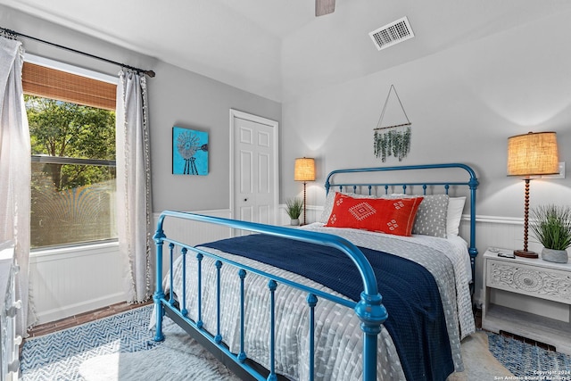 bedroom with a wainscoted wall, visible vents, ceiling fan, and wood finished floors