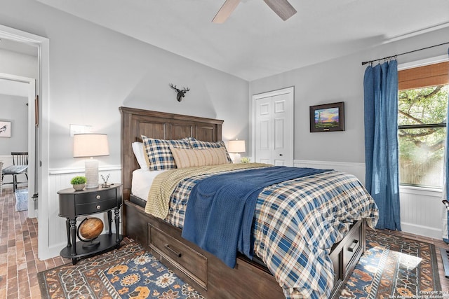 bedroom featuring a wainscoted wall, ceiling fan, a closet, and brick floor