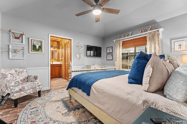 bedroom with a wainscoted wall, lofted ceiling, ensuite bathroom, a ceiling fan, and wood finished floors