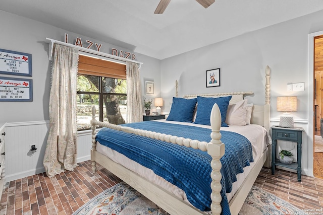 bedroom featuring brick floor, wainscoting, and ceiling fan