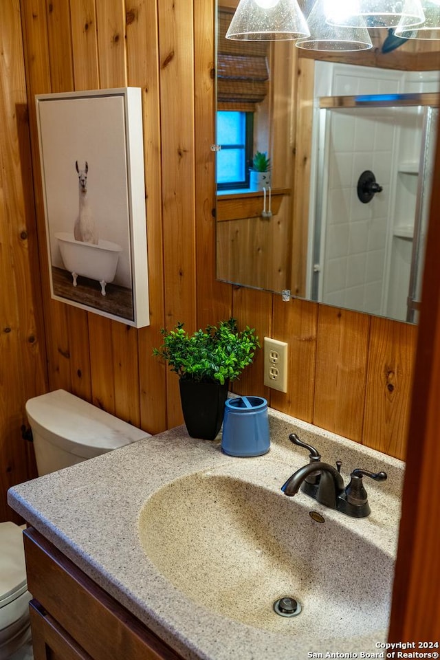 bathroom featuring wood walls, a shower stall, toilet, and vanity