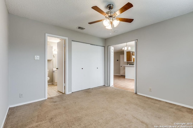 unfurnished bedroom with ensuite bathroom, light colored carpet, a textured ceiling, a closet, and ceiling fan with notable chandelier