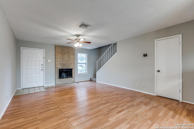 unfurnished living room featuring ceiling fan, a brick fireplace, a textured ceiling, and light hardwood / wood-style floors