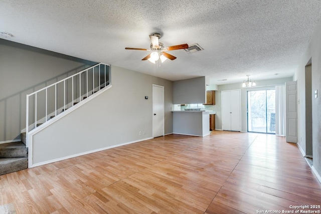 unfurnished living room with a textured ceiling, ceiling fan with notable chandelier, and light hardwood / wood-style floors