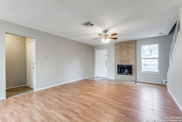 unfurnished living room with a brick fireplace, light hardwood / wood-style floors, a textured ceiling, and ceiling fan