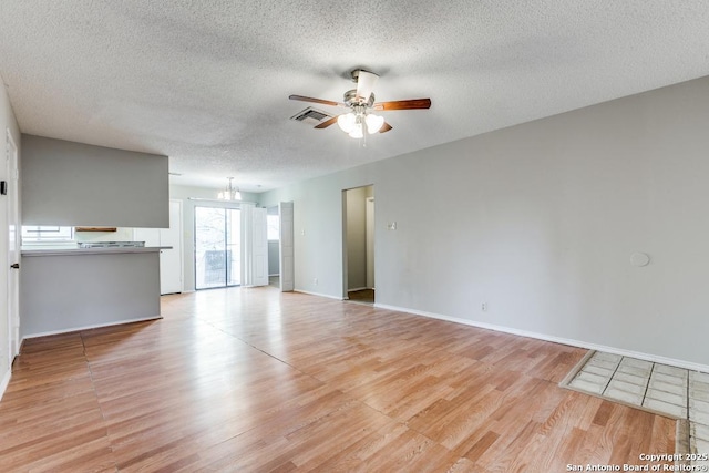 unfurnished living room with ceiling fan with notable chandelier, a textured ceiling, and light wood-type flooring