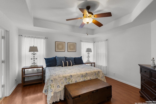 bedroom featuring ceiling fan, dark hardwood / wood-style floors, and a tray ceiling