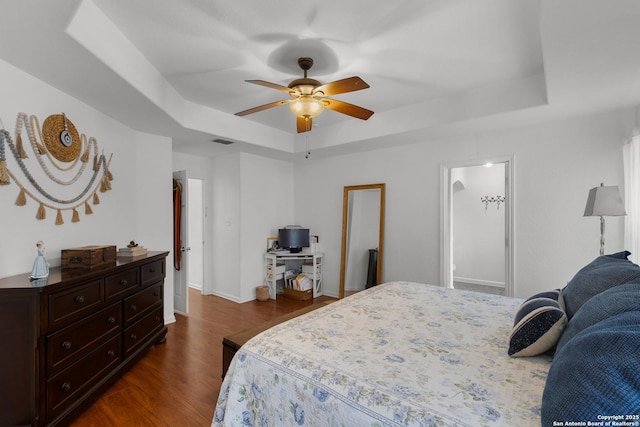 bedroom with ceiling fan, dark hardwood / wood-style floors, and a tray ceiling