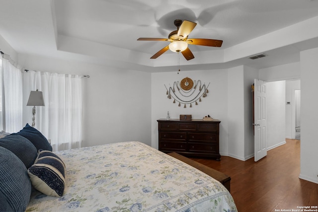 bedroom with dark wood-type flooring, ceiling fan, and a tray ceiling