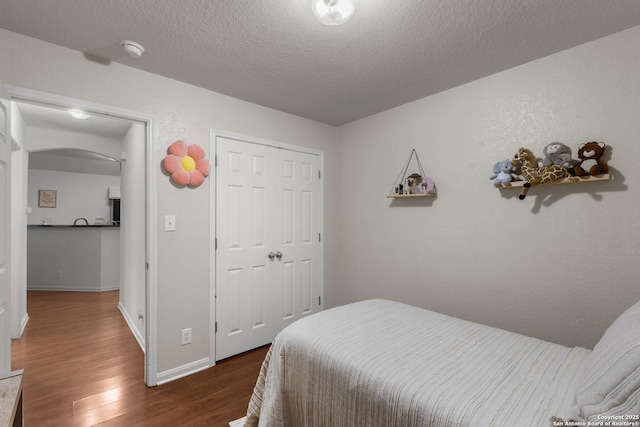 bedroom with a textured ceiling, dark wood-type flooring, and a closet