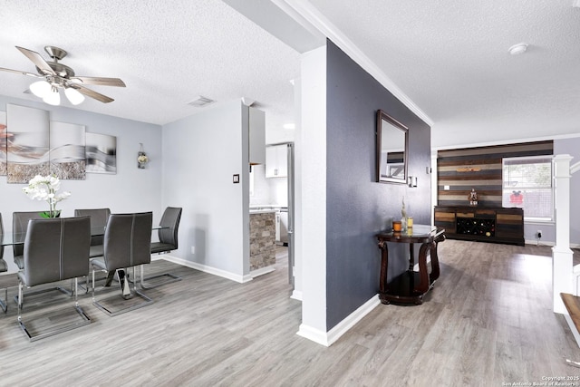 dining room with ceiling fan, a textured ceiling, ornamental molding, and light wood-type flooring