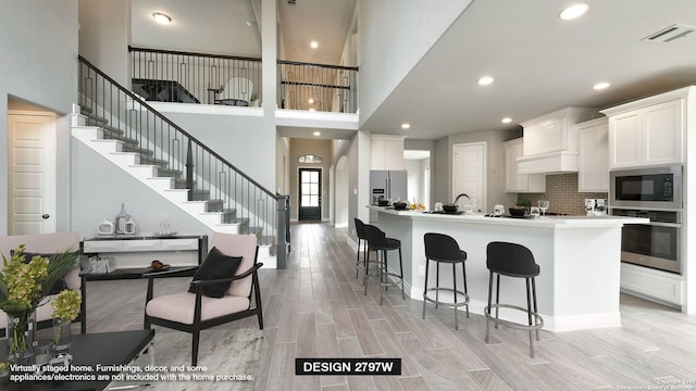 kitchen with white cabinetry, appliances with stainless steel finishes, backsplash, a kitchen island with sink, and a kitchen breakfast bar