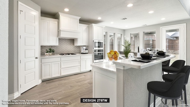 kitchen featuring appliances with stainless steel finishes, white cabinetry, an island with sink, tasteful backsplash, and a breakfast bar