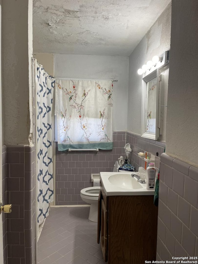 bathroom with a textured ceiling, tile patterned flooring, tile walls, and vanity