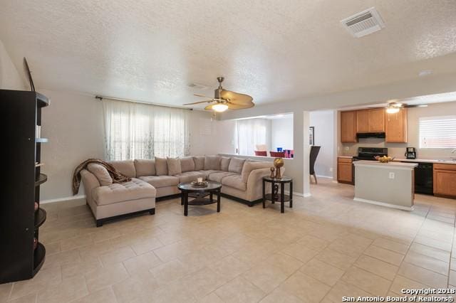 living room with ceiling fan, a textured ceiling, and a healthy amount of sunlight