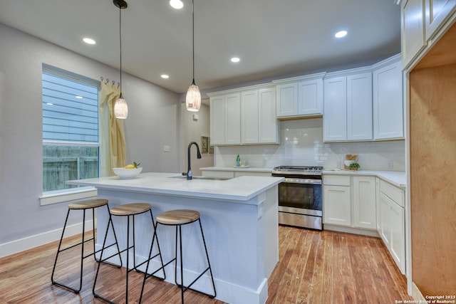 kitchen featuring a center island with sink, stainless steel gas range, hanging light fixtures, white cabinets, and sink