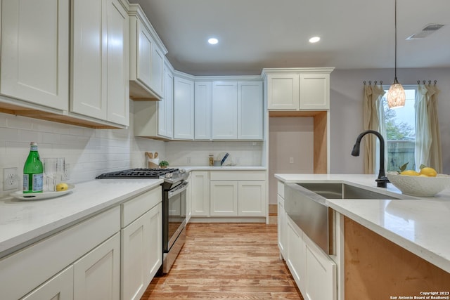 kitchen featuring light stone counters, stainless steel range with gas cooktop, white cabinetry, and decorative light fixtures