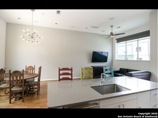 kitchen featuring ceiling fan with notable chandelier, light hardwood / wood-style floors, white cabinets, and sink