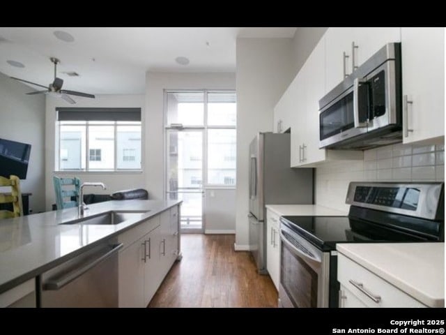 kitchen with tasteful backsplash, sink, white cabinetry, dark wood-type flooring, and appliances with stainless steel finishes